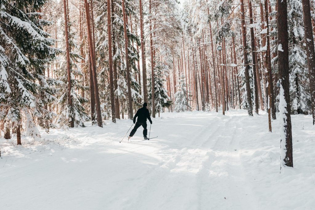 Mies mustassa asussa hiihtää lumisessa metsässä.